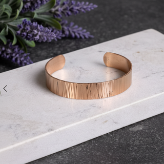 Rose gold bracelet on a marble surface with lavender flowers in the background