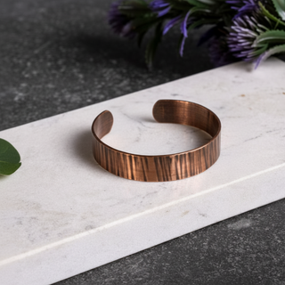 Copper bracelet on a marble surface with purple flowers in the background