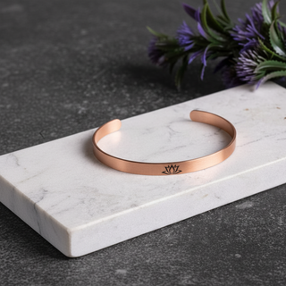 Rose gold bracelet on a marble surface with purple flowers in the background