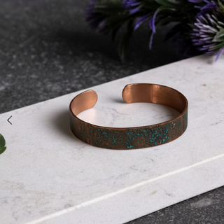 Copper bracelet with speckled pattern on a marble surface with purple flowers in the background