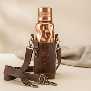 Copper water bottle in a leather holder with a strap on a beige background